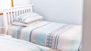 A neatly made bed with a striped blanket and pillows, a bedside table with a lamp, and a white headboard.