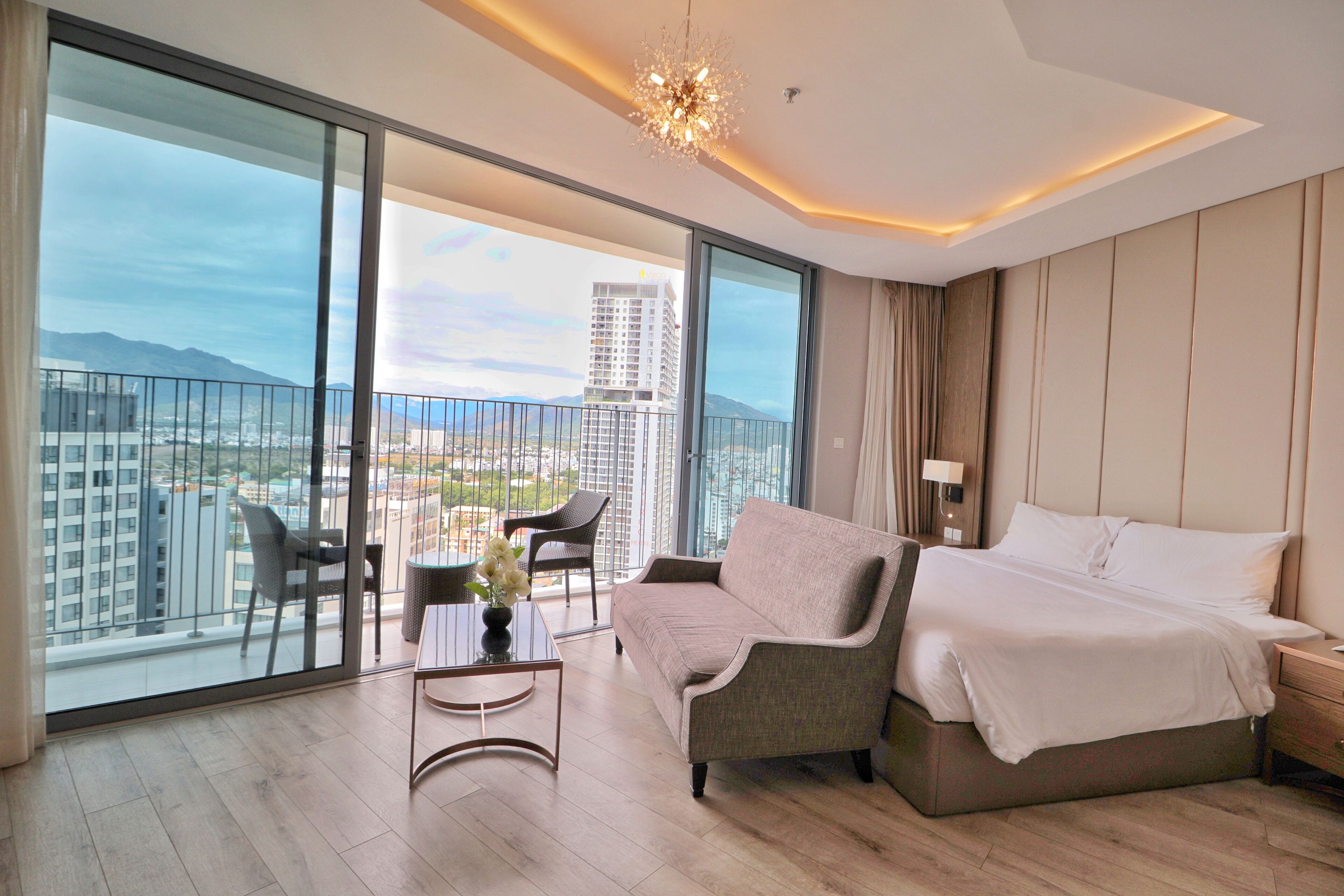 Habitación de hotel moderna con balcón, sofá, cama y una mesa con un florero.