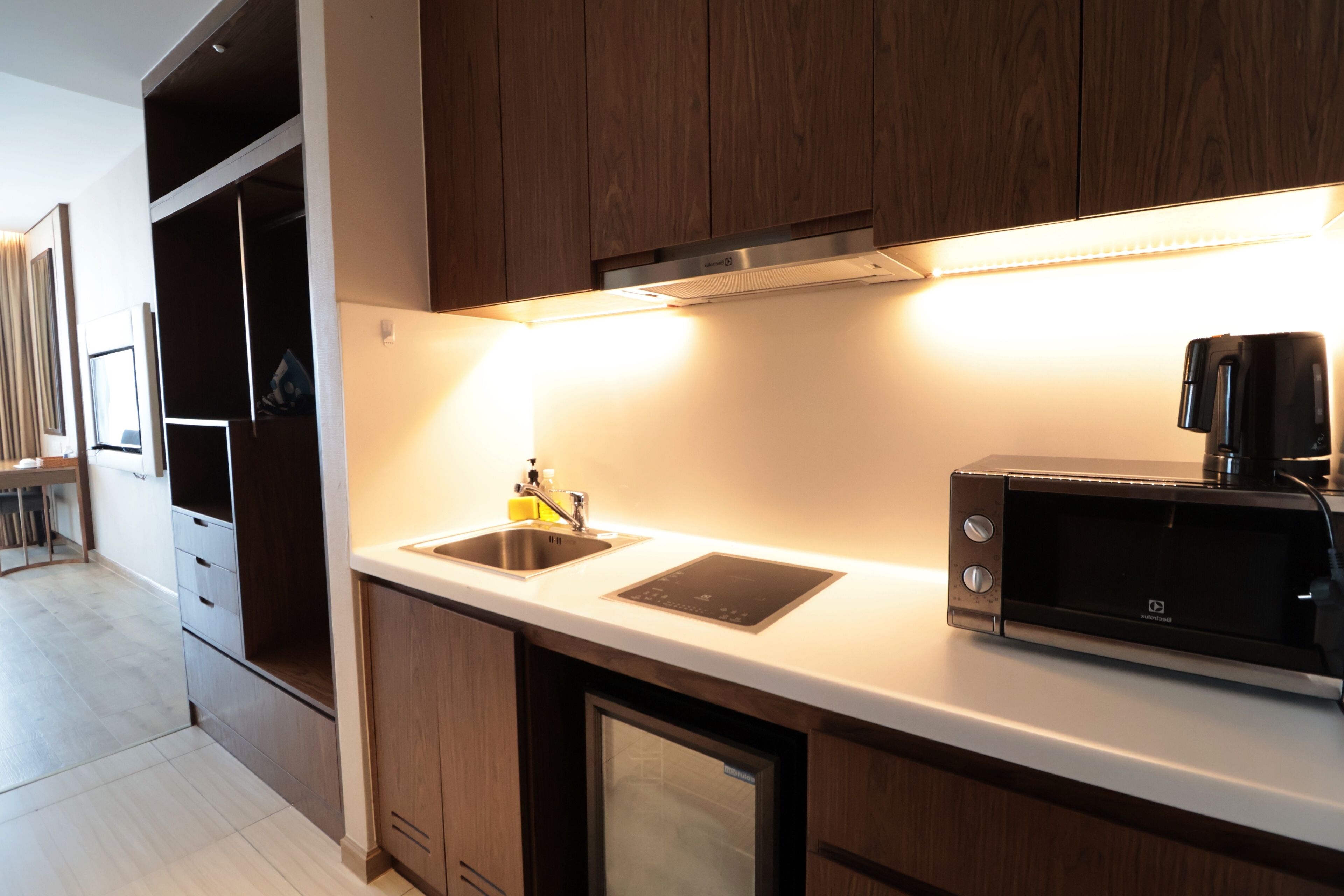 Una cocina moderna con armarios de madera, microondas integrado y un lavamanos de acero inoxidable.