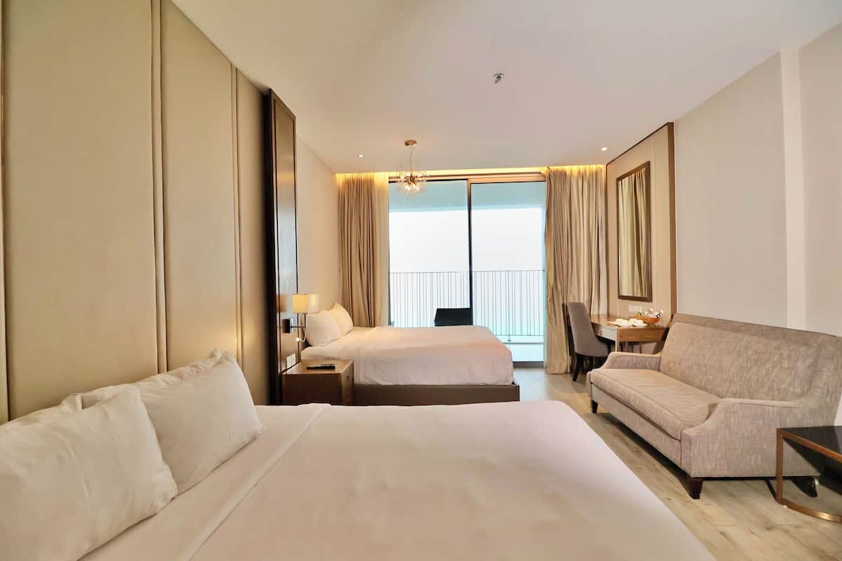A hotel room with two beds, a sofa, a desk, and a chair.