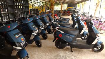 Una fila de scooters azules estacionados en un área techada con piso de concreto.
