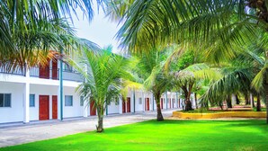 A courtyard with a white building, palm trees, and a green lawn. - ReeCha Mullai Resort (Iyakachchi)