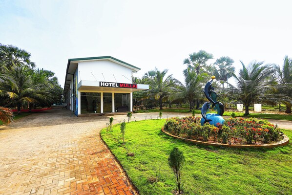 A hotel building with a sign reading 'HOTEL MULLAI' and a sculpture of a person playing a guitar in the garden.