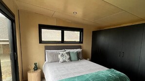 A modern bedroom with a bed, a window, a wardrobe, and a small side table. - Tranquility - Rural Location (Horse Friendly) (Ohinewai)
