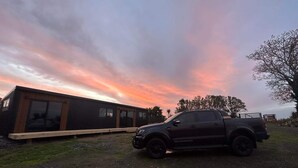 A modern building with large windows and a vehicle parked in front. - Tranquility - Rural Location (Horse Friendly) (Ohinewai)