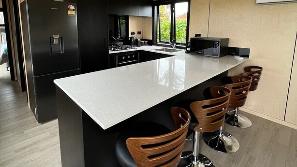 A modern kitchen with a large island, black cabinetry, and wooden bar stools. - Tranquility - Rural Location (Horse Friendly) (Ohinewai)