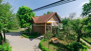 A small brick house with a tiled roof, surrounded by greenery and a paved driveway. - SƠN HOME GARDEN HUE (Hue)