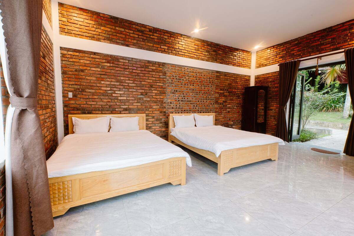 A room with two wooden beds, a brick wall, and a large window with curtains.