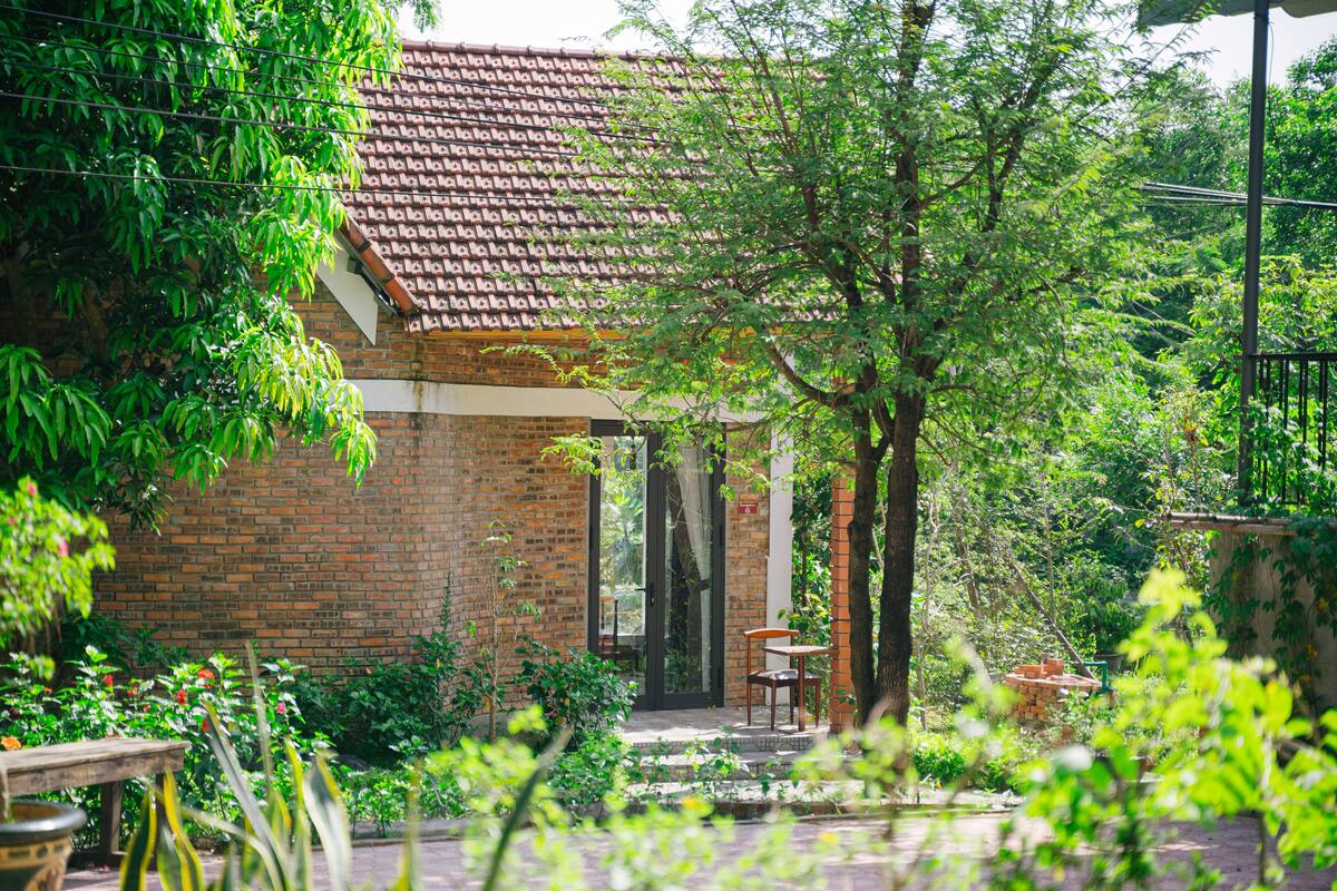 A brick building with a tiled roof, surrounded by lush greenery and a small outdoor seating area.