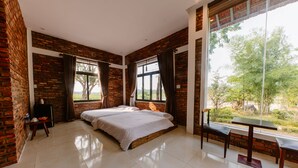 A bedroom with a large bed, a desk, and a view of a garden through large windows. - SƠN HOME GARDEN HUE (Hue)