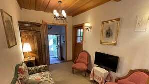 Een gezellige woonkamer met een bloemenbank, een roze fauteuil, een televisie en een houten plafond.
