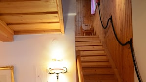 Een houten trap met een leuning, een stoel, een tafel met een afstandsbediening, en een wandlamp.