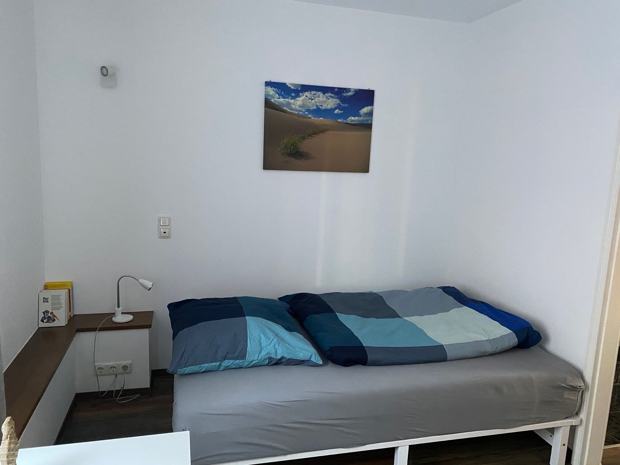 Un dormitorio con una cama, una mesita de noche, una lámpara y un cuadro de un paisaje desértico.