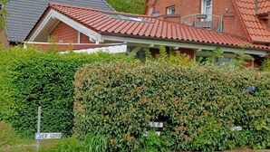 A two-story house with a red-tiled roof, a visible garage door, and a well-maintained hedge in front. - Moderne Ferienwohnung 90qm, mit Garten in Wesernähe - Nähe Golfplatz (Achim)