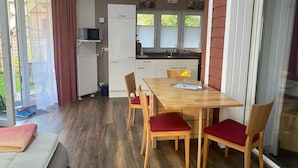 A compact kitchen with a refrigerator, microwave, and sink. There is a dining table with chairs and a small window with blinds. - Moderne Ferienwohnung 90qm, mit Garten in Wesernähe - Nähe Golfplatz (Achim)