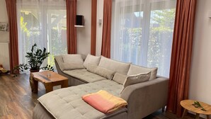 A modern living room with a sofa, a small table, and a potted plant. - Moderne Ferienwohnung 90qm, mit Garten in Wesernähe - Nähe Golfplatz (Achim)