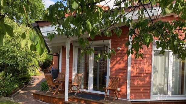 A red brick house with a covered porch, two wooden chairs, and a blue mat. - Moderne Ferienwohnung 90qm, mit Garten in Wesernähe - Nähe Golfplatz (Achim)
