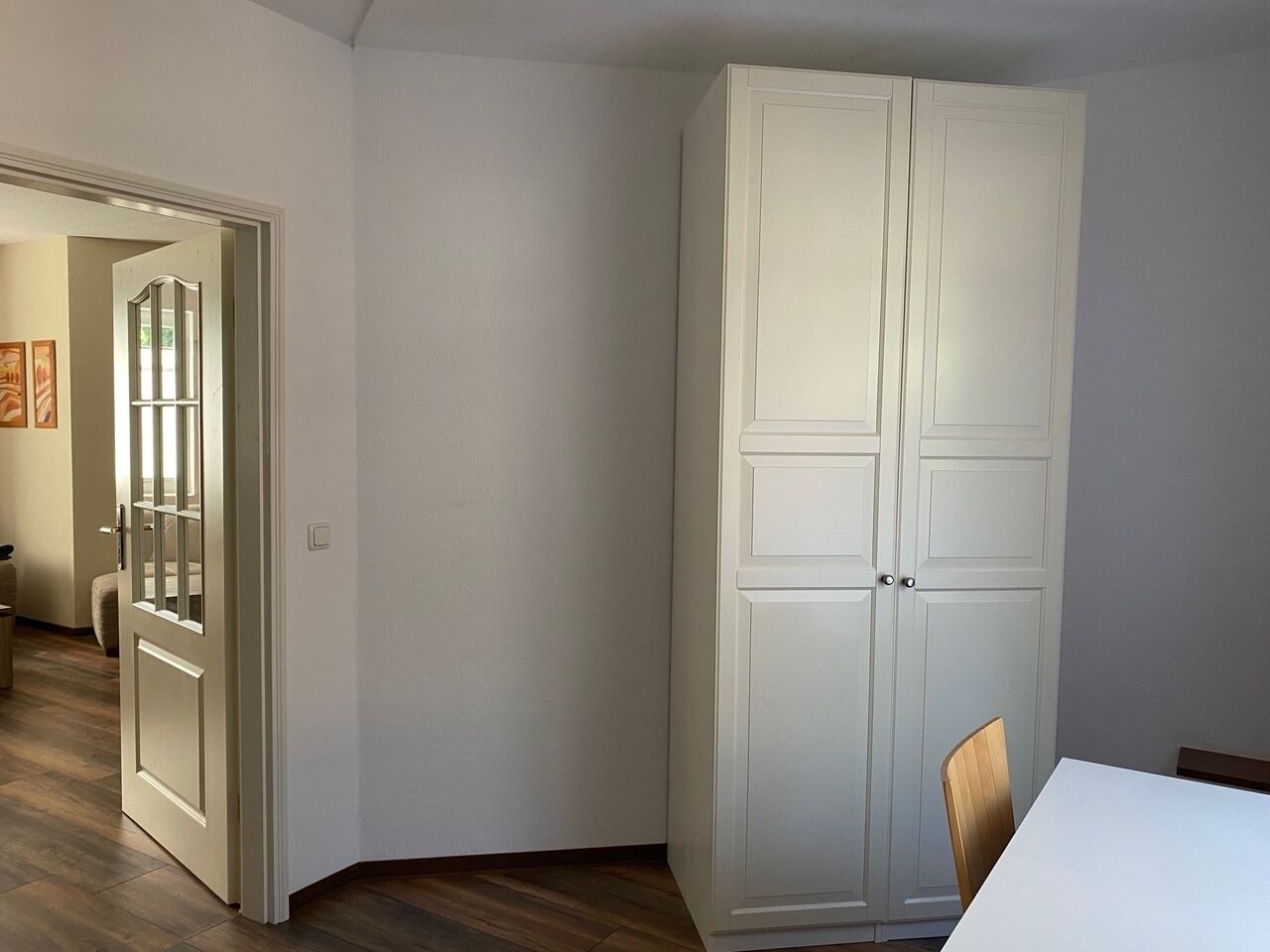 Una habitación con un armario blanco, suelo de madera y una puerta que da a otra estancia.