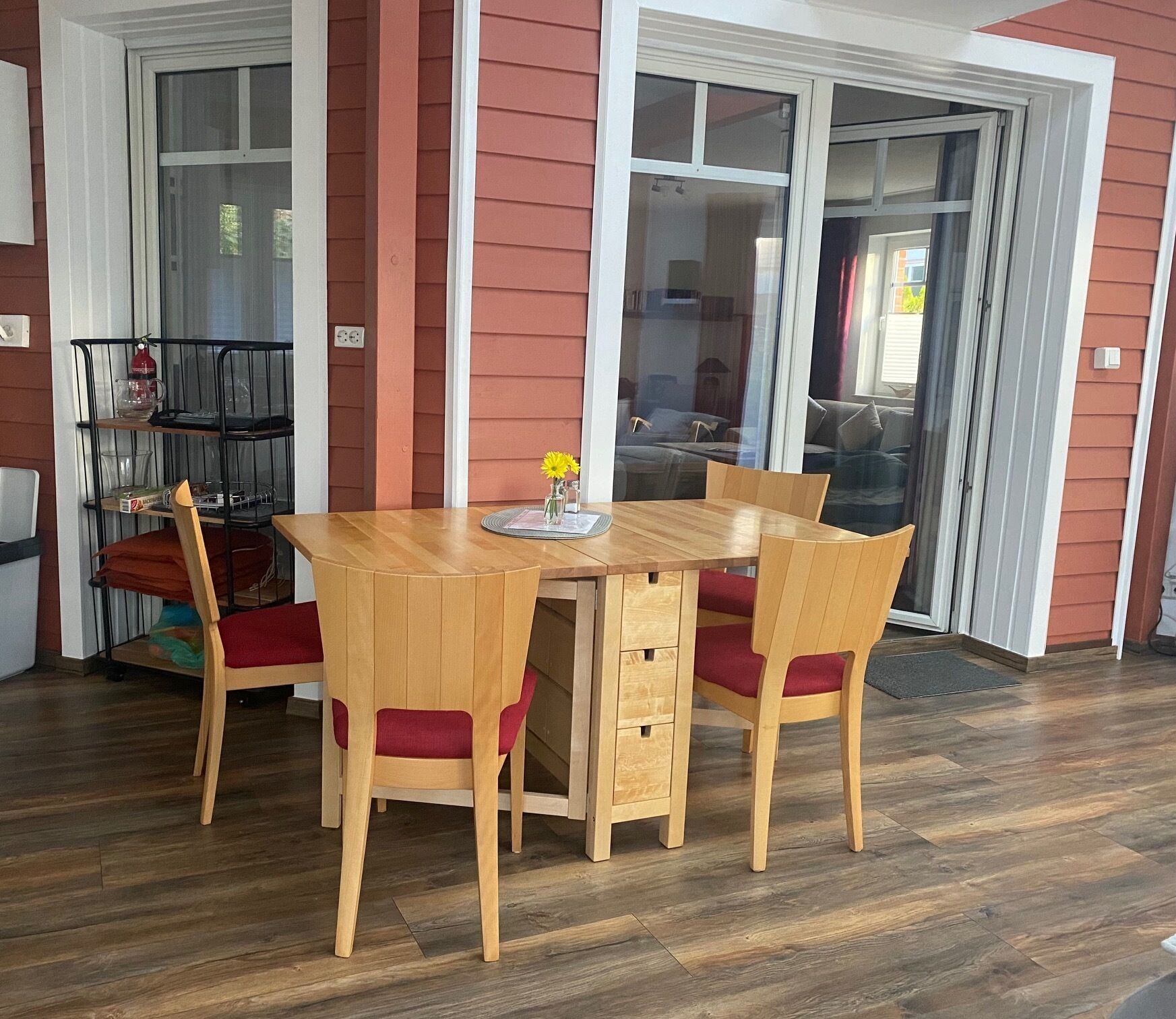 Un coin repas avec une table et des chaises en bois, un petit vase avec des fleurs et une porte-fenêtre coulissante donnant sur le salon.