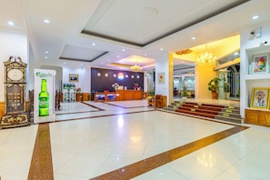 A hotel lobby with a reception desk, a clock, and a large green bottle of Carlsberg beer. - Lisha roungnakhone hotel (Vang Vieng)