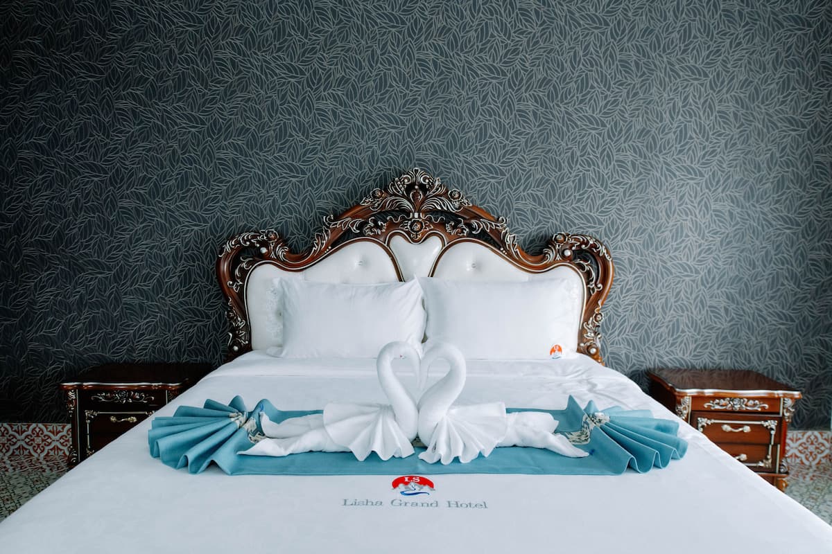 Ein Bett mit weißem Kopfteil, zwei Kissen und einer dekorativen Schwananordnung auf der Tagesdecke.