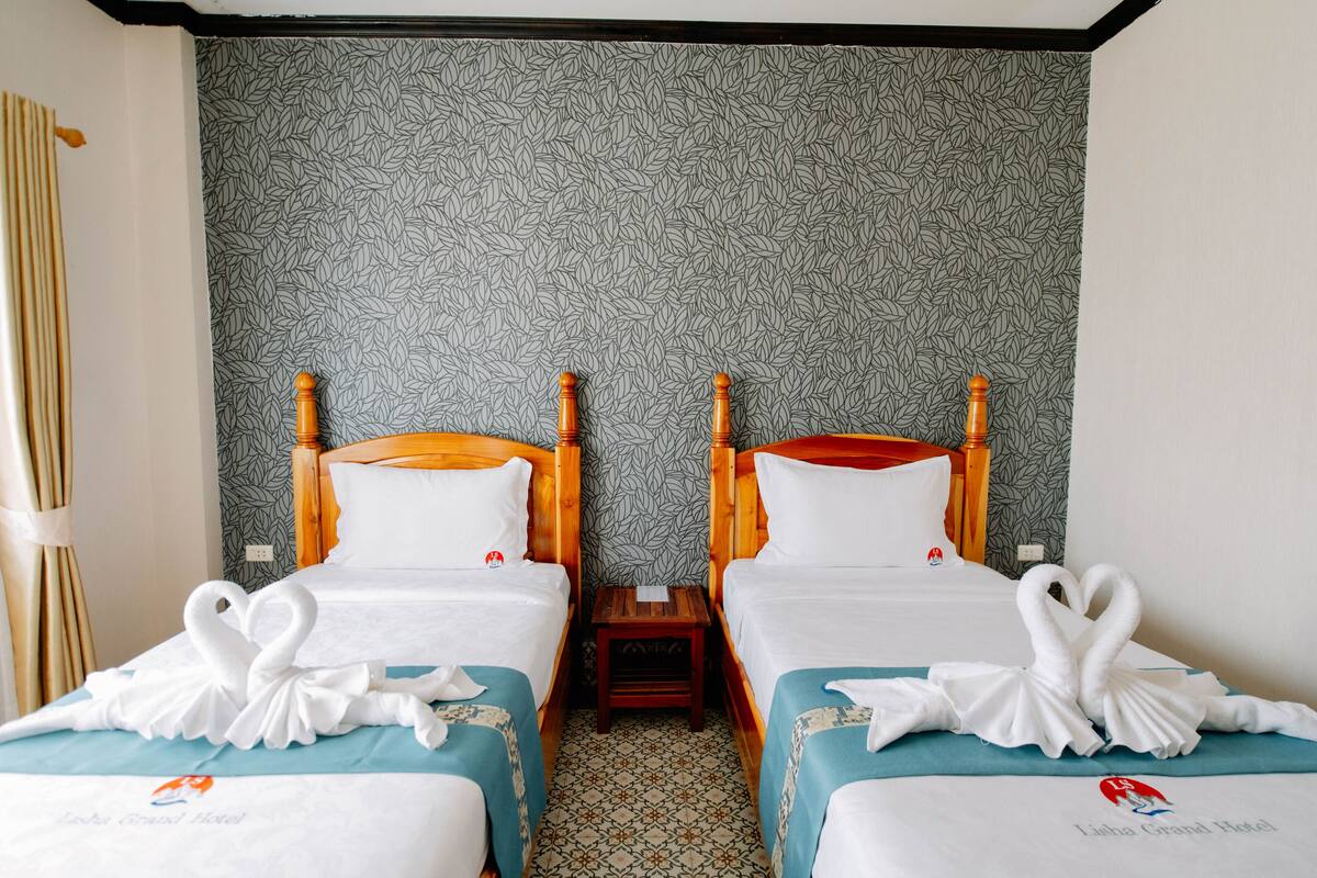 Ein Hotelzimmer mit zwei Betten, einem gemusterten Wandteppich und einem kleinen Holztisch.