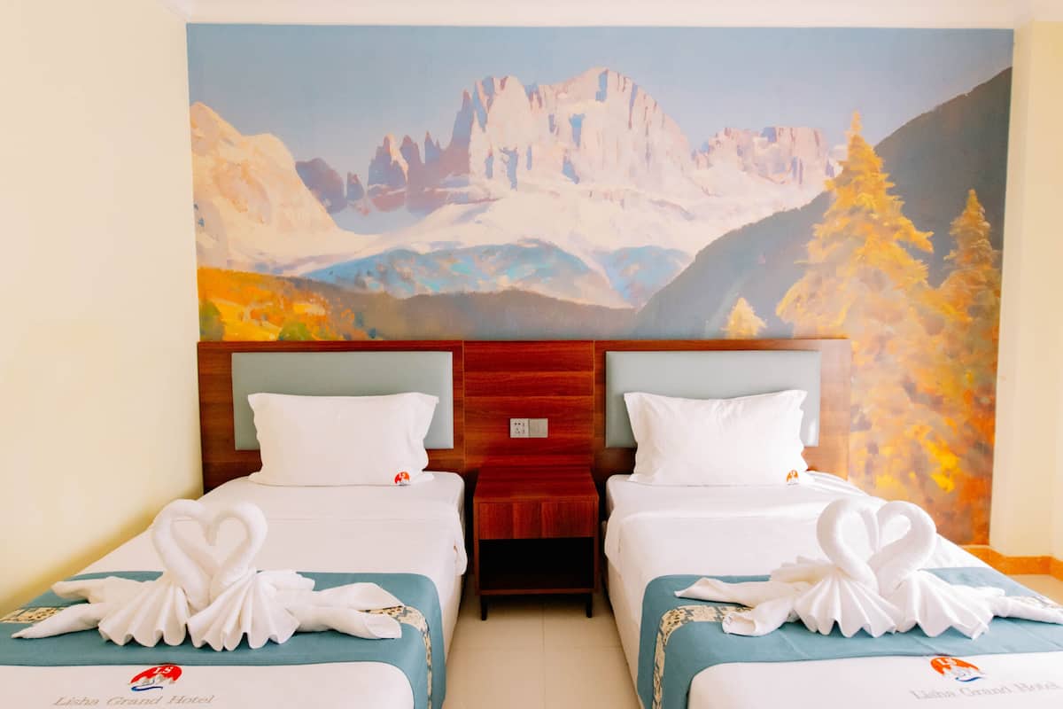 Ein Hotelzimmer mit zwei Betten, jedes mit einem herzförmigen Handtuch, einer Bergwandmalerei und einem Holzkopfteil.