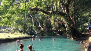 Un cos d'aigua natural envoltat d'arbres, amb persones nedant i assegudes a cadiretes.