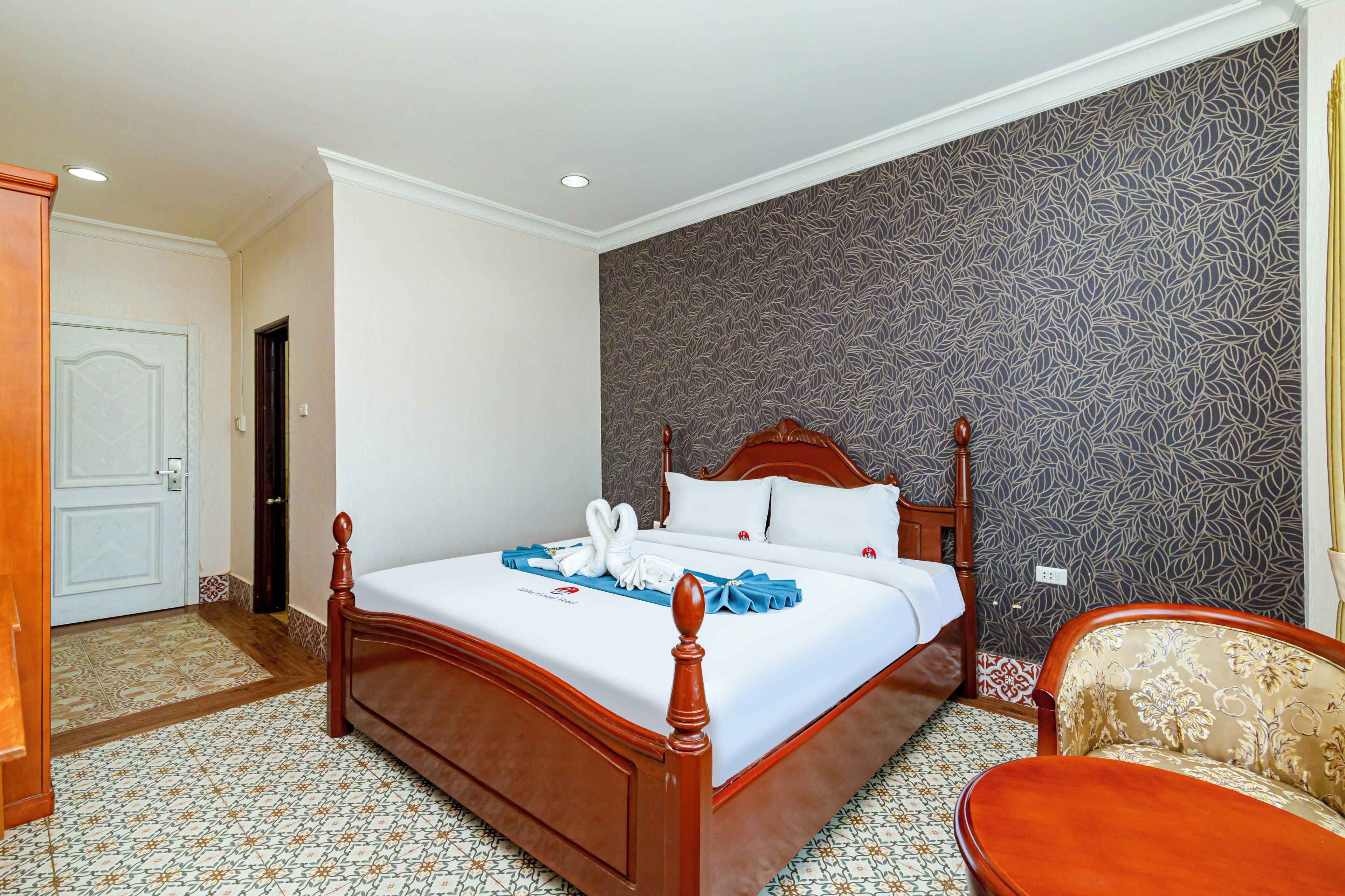 Una habitación de hotel con una cama de madera, un papel tapiz estampado, una silla y una puerta.