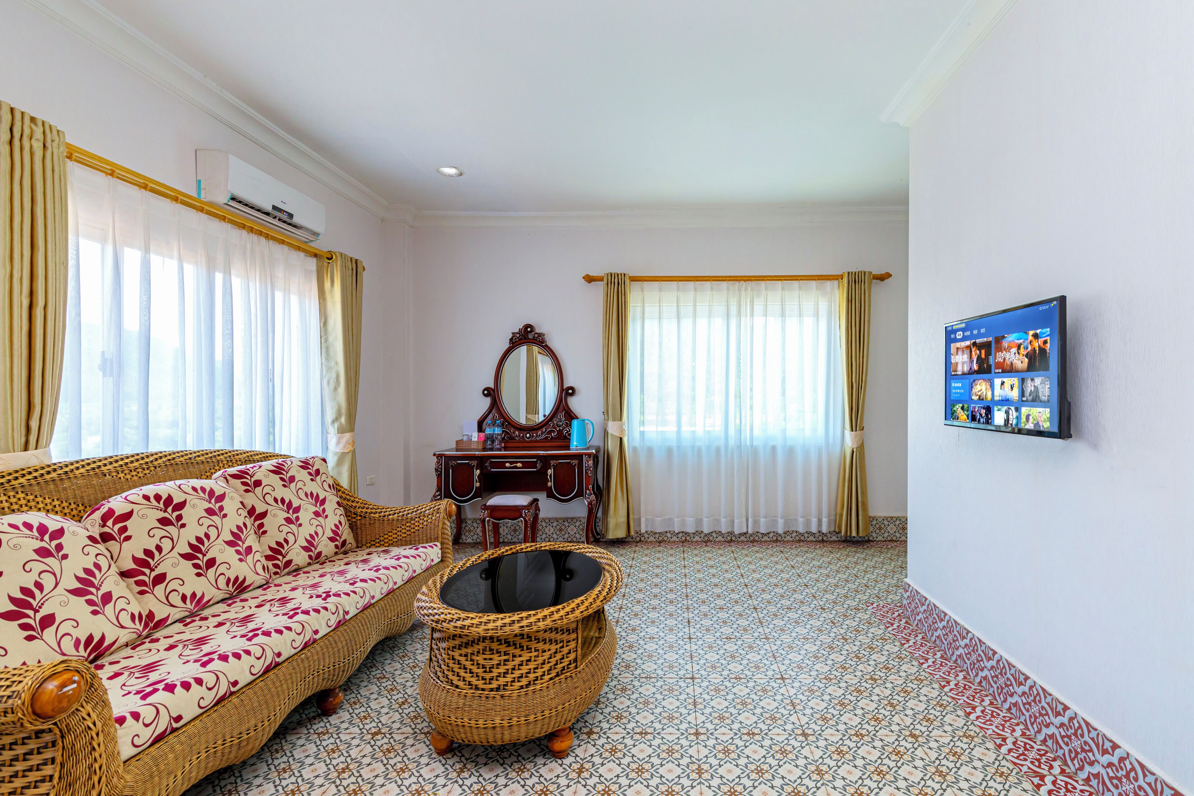 A room with a sofa, a small table, a decorative mirror, a wall-mounted TV, and a patterned floor.