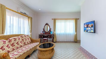 Una habitación con un sofá, una mesita, un espejo decorativo, un televisor montado en la pared y un suelo estampado.
