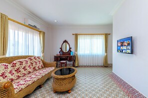 A room with a sofa, a small table, a decorative mirror, a wall-mounted TV, and a patterned floor. - Lisha roungnakhone hotel (Vang Vieng)