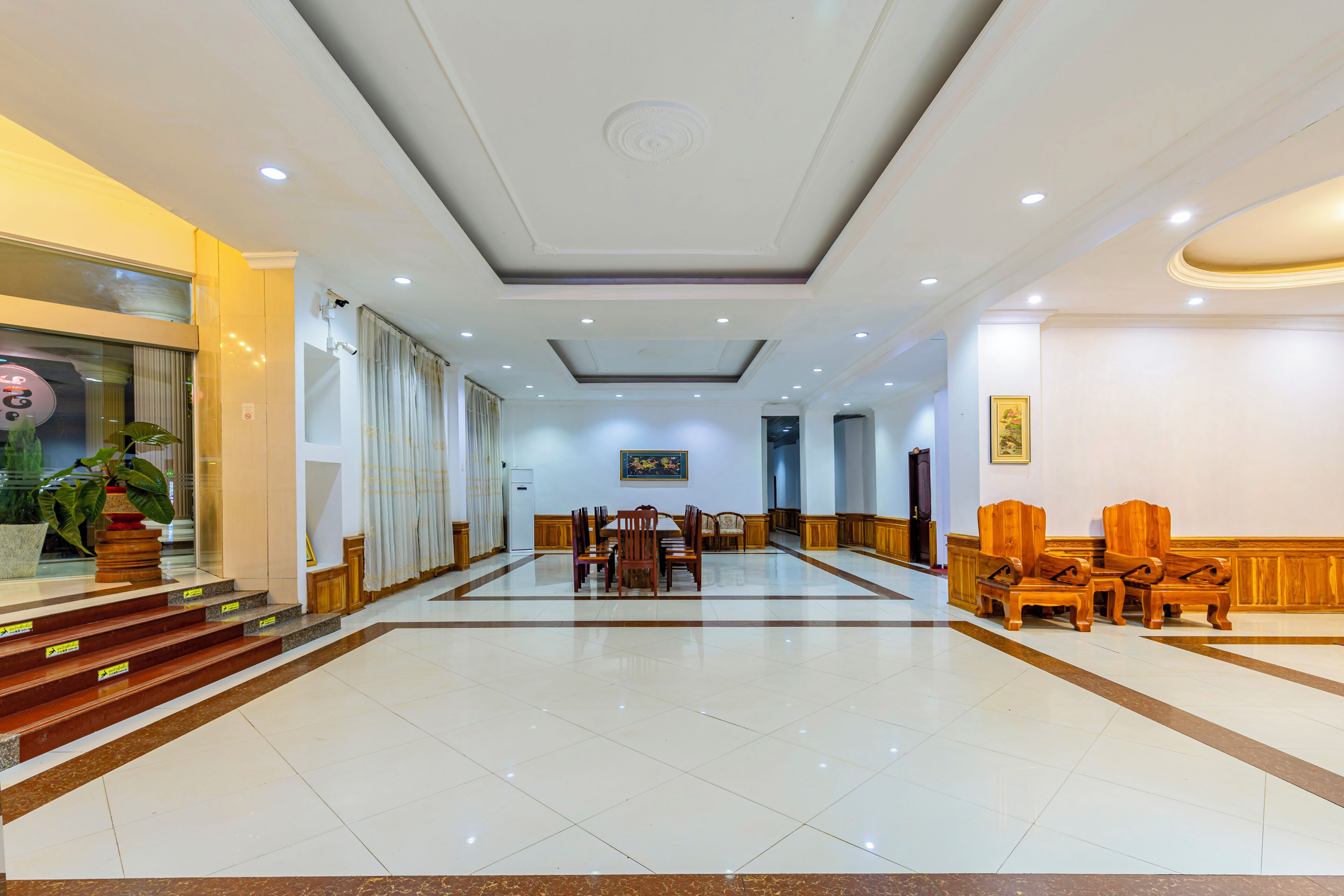 Eine Hotelhalle mit einer zentralen Essecke, einer Treppe zum Obergeschoss und einer Rezeption.