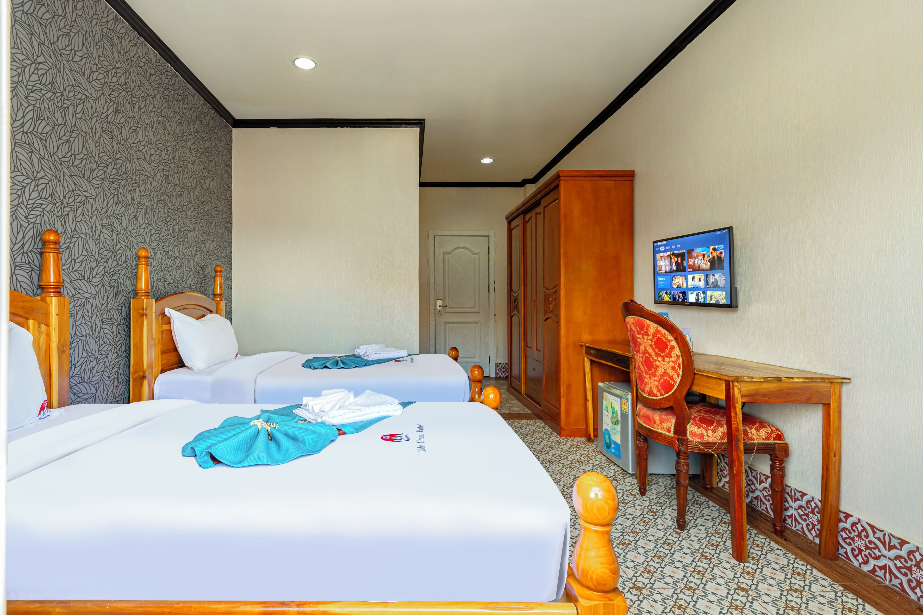 Een hotelkamer met twee bedden, een bureau, een stoel en een televisie aan de muur.