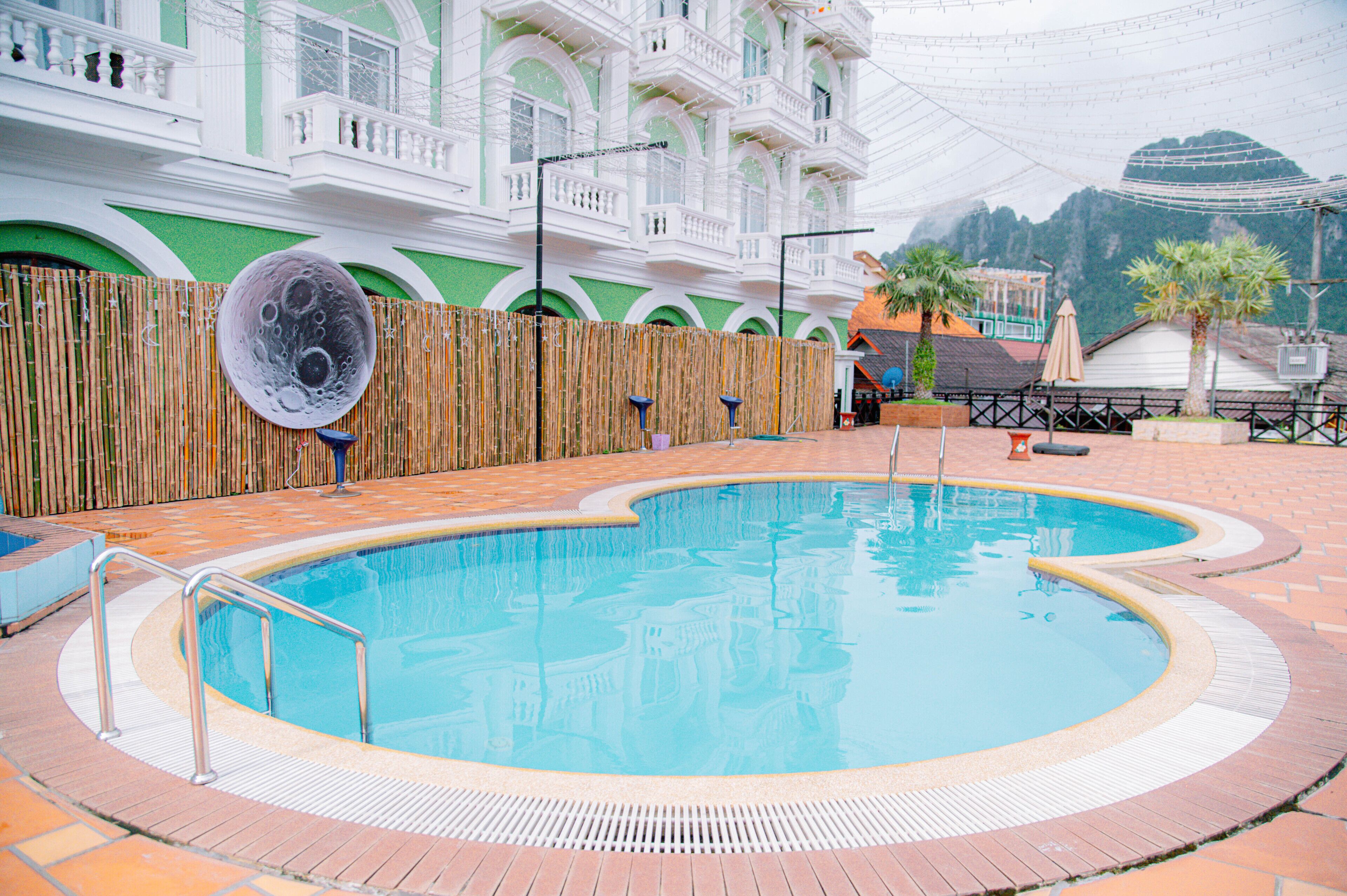 Una piscina con valla de bambú, un edificio con balcones y una montaña al fondo.