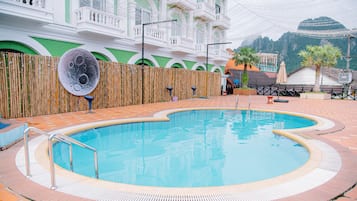 Una piscina con valla de bambú, un edificio con balcones y una montaña al fondo.