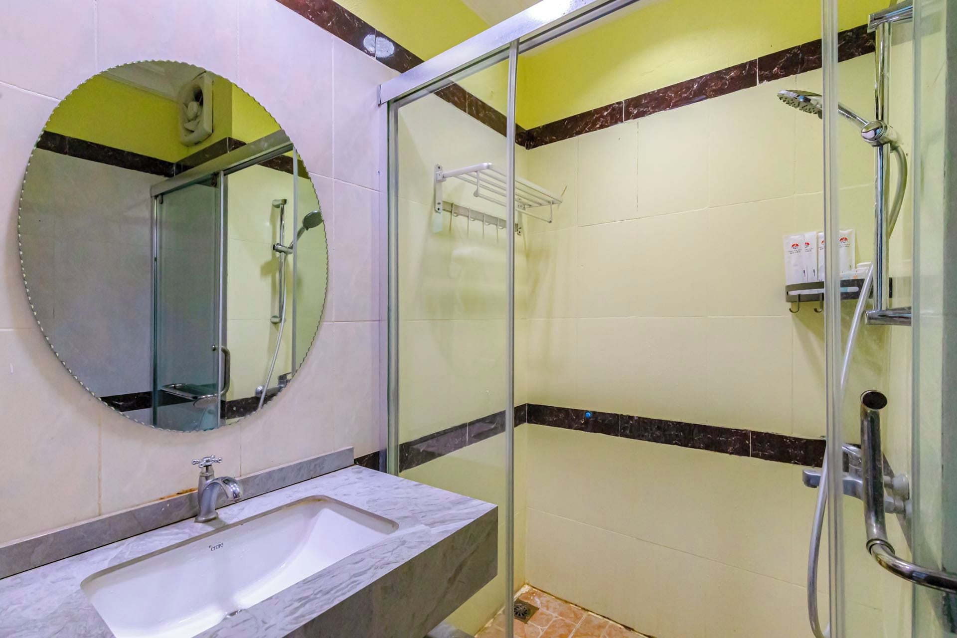 Une salle de bain dotée d’une douche à parois de verre, d’un lavabo avec un plan de travail en marbre et d’un miroir à cadre circulaire.