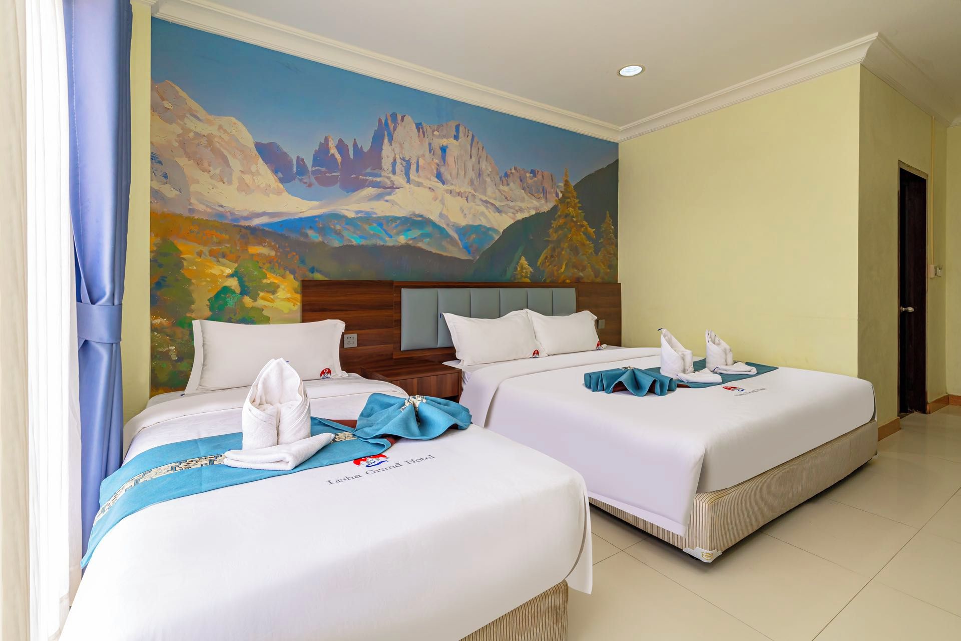 Habitación de hotel con dos camas, un mural de paisaje montañoso y una placa en la cabecera.