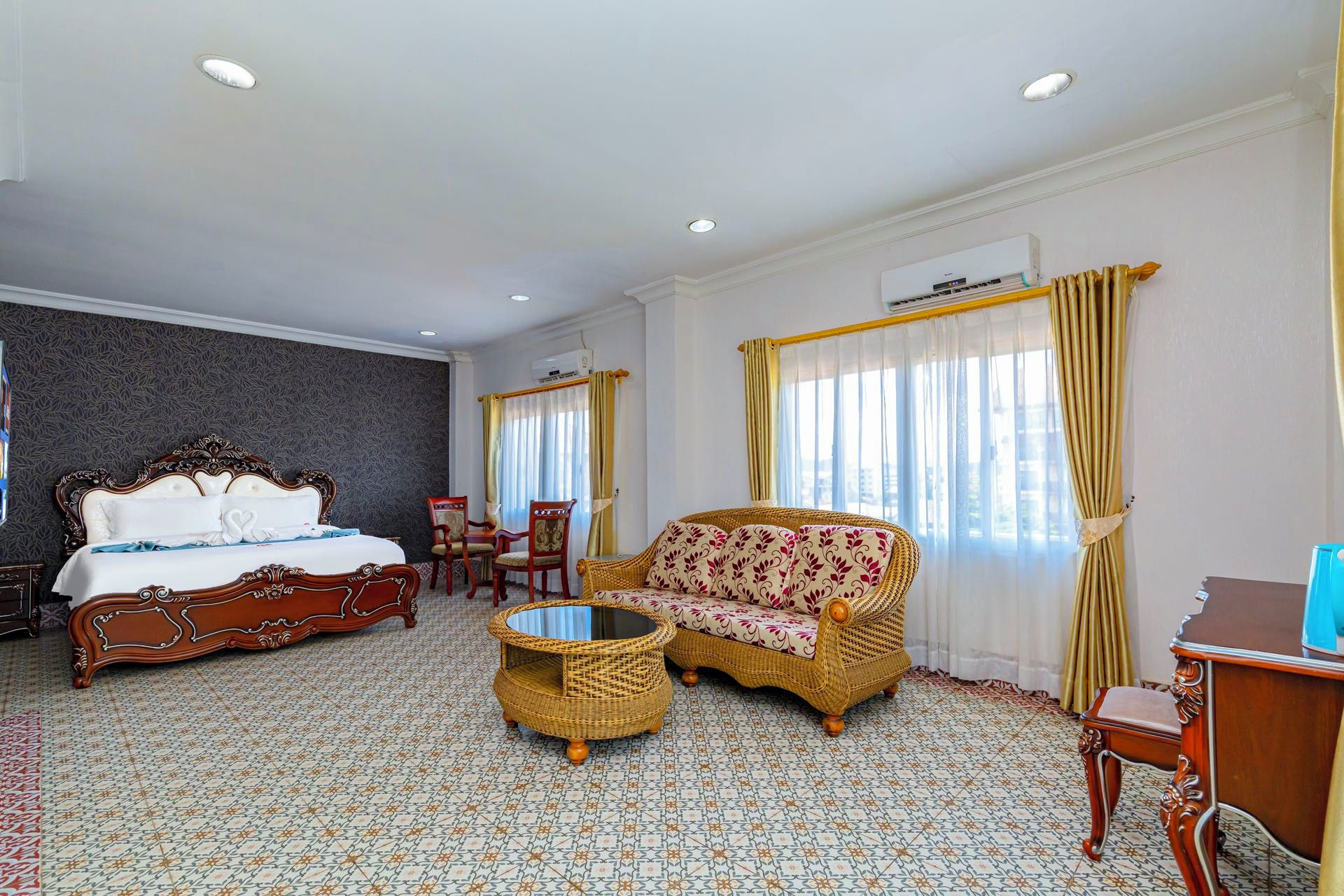 A hotel room with a large bed, a sofa, a small table, and a chair.