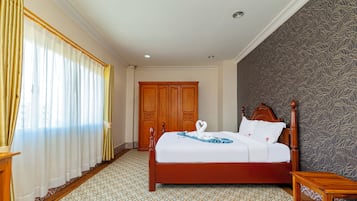 Een hotelkamer met een bed, een houten garderobe, een vloer met een patroon en een raam met gordijnen.