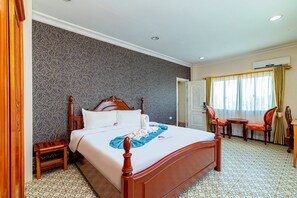 Ein Hotelzimmer mit einem großen Bett, einem Holzkopfende, einem Nachttisch, einem Stuhl, einem Schreibtisch und einem Fenster mit Vorhängen.