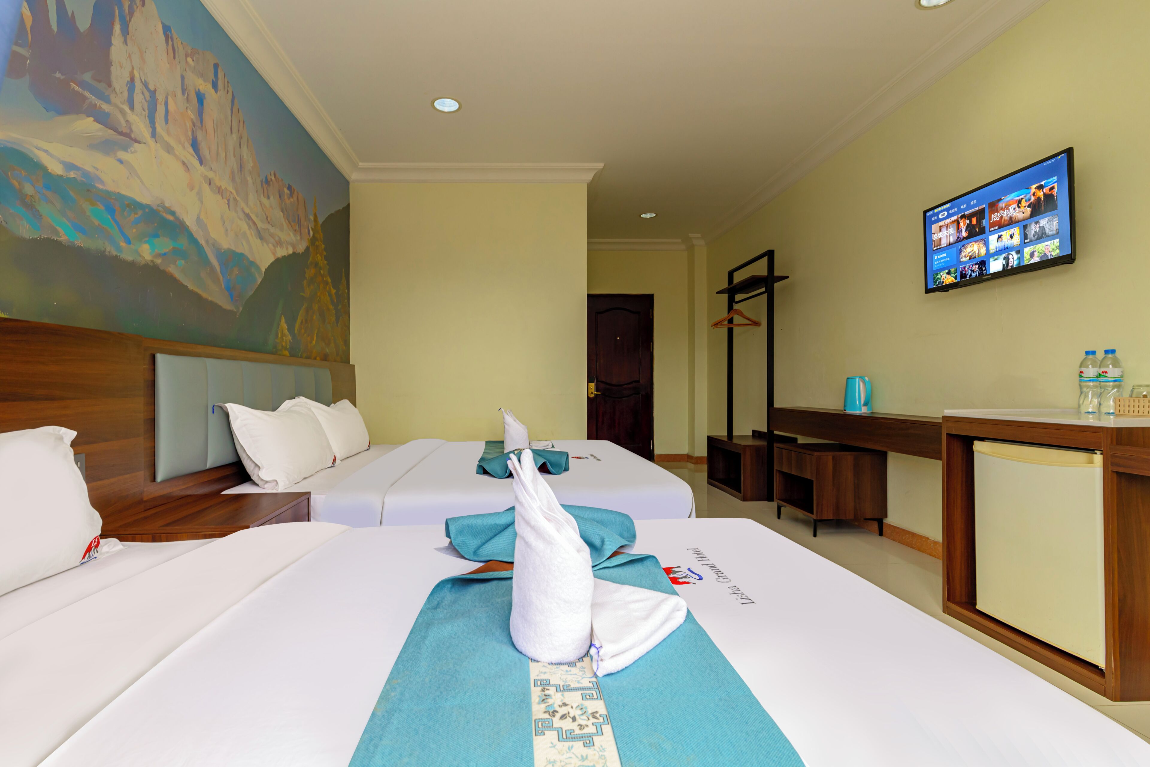 A hotel room with two beds, a television on the wall, and a painting on the wall.
