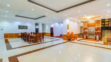 A spacious lobby with a marble floor, wooden furniture, and a reception area with a marble counter and elevator.