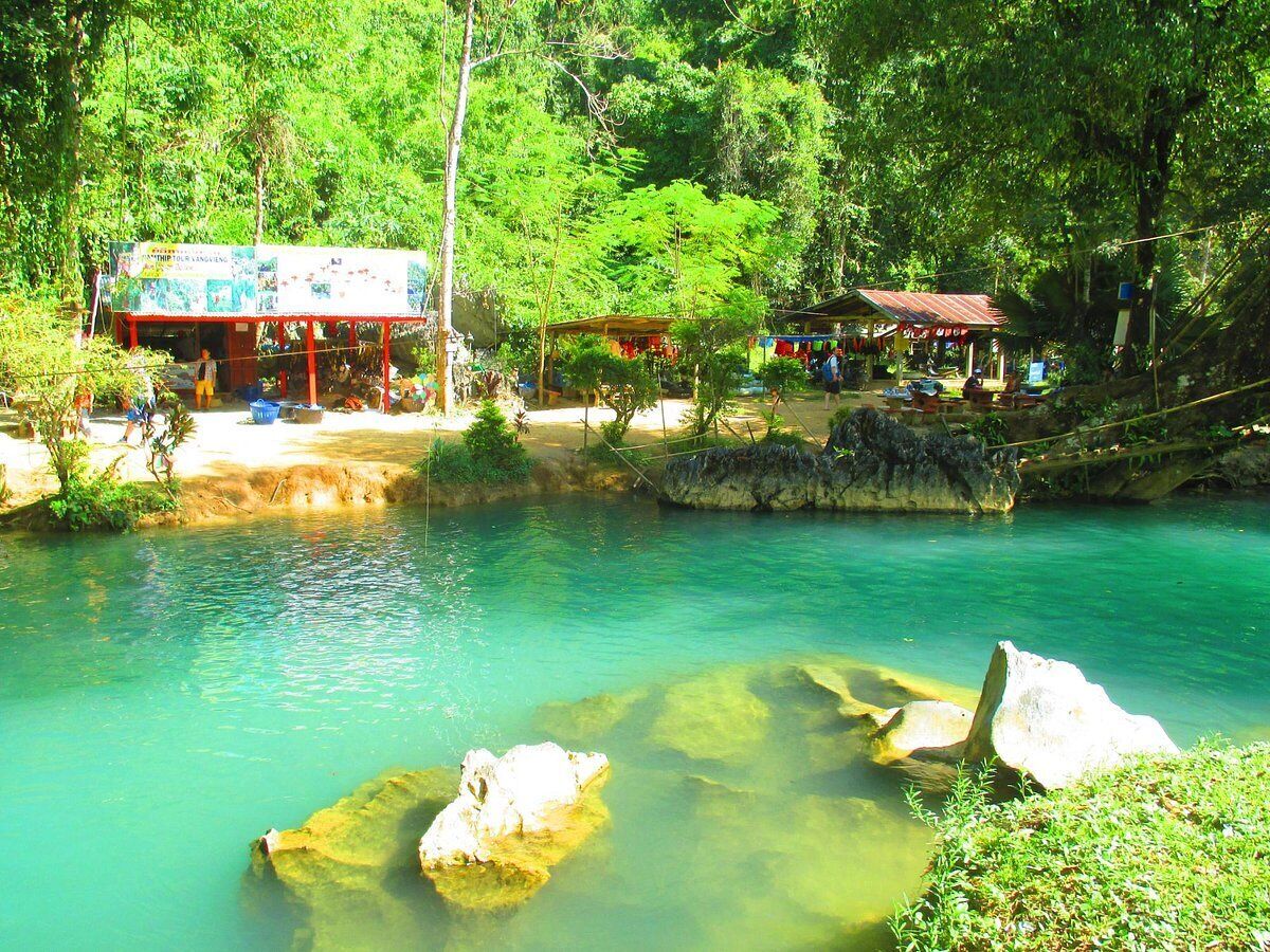 A natural pool surrounded by lush greenery and a small building with a red roof.