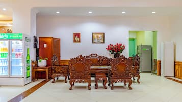 Vestíbulo de hotel con mostrador de recepción, refrigerador, máquina expendedora y zona de comedor con muebles de madera ornamentada.