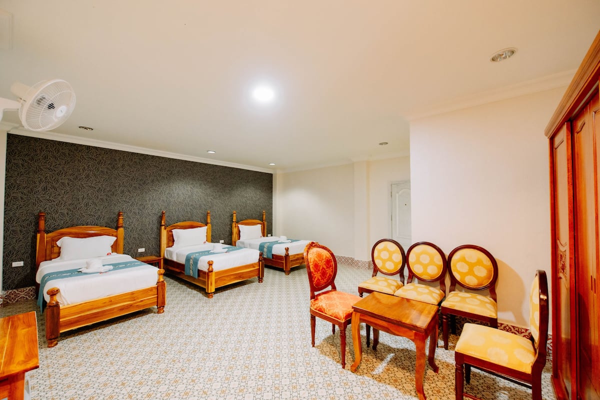 Ein Hotelzimmer mit vier Holzbett, einem Esstisch mit Stühlen, einem Ventilator und einem Kleiderschrank.