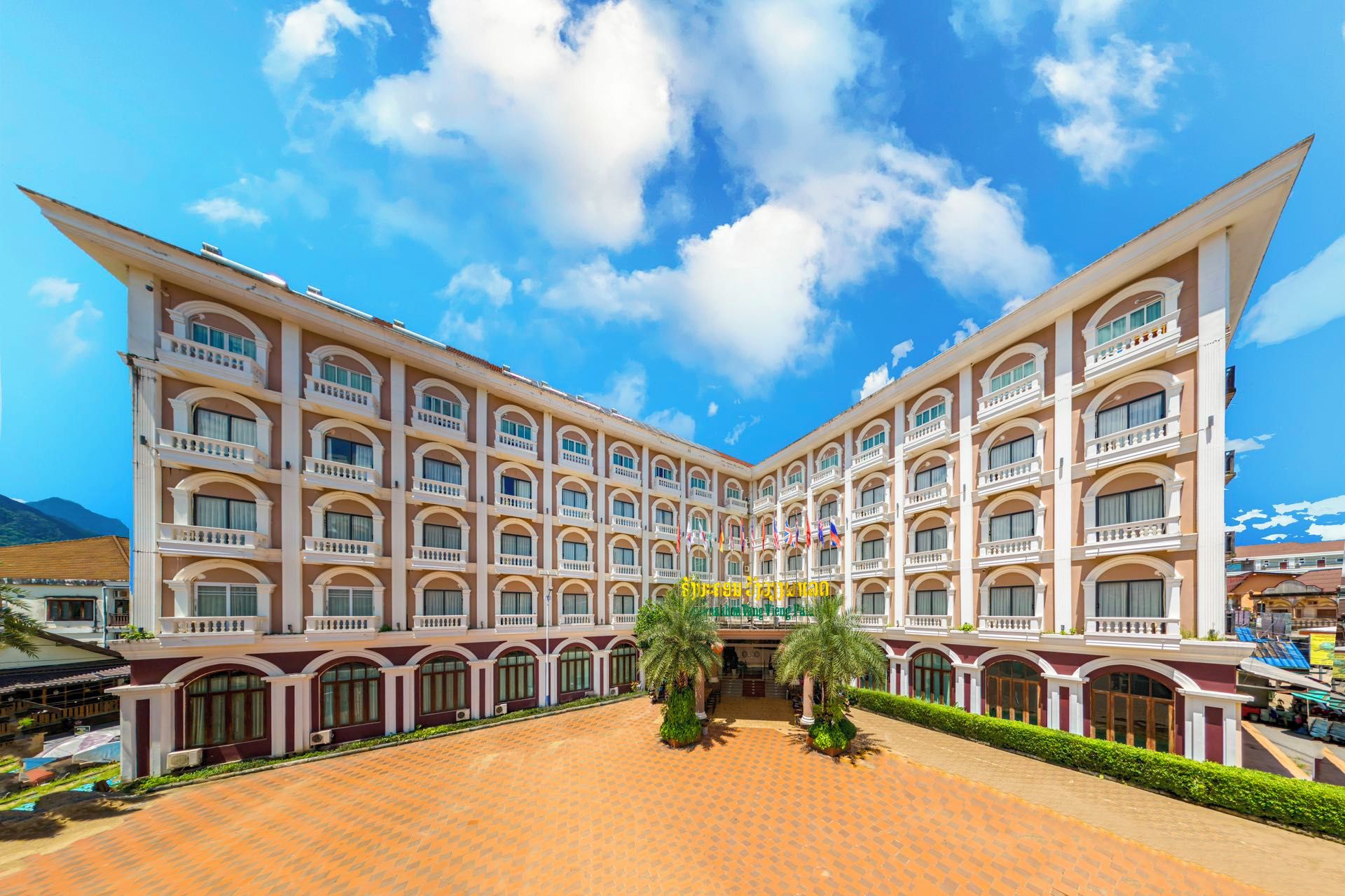 Un hôtel à plusieurs étages, doté d’une façade symétrique, de nombreux balcons et d’une cour intérieure agrémentée de palmiers.