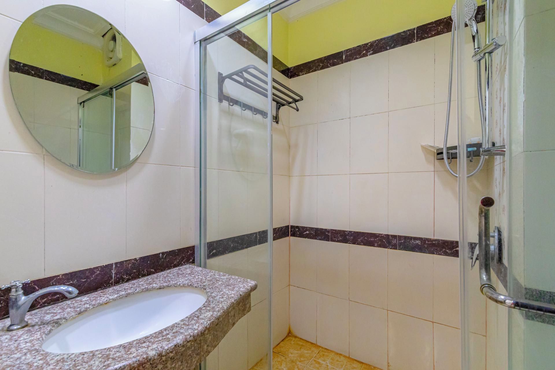 Un baño con lavamanos de encimera de granito, cabina de ducha de vidrio y un espejo en la pared.