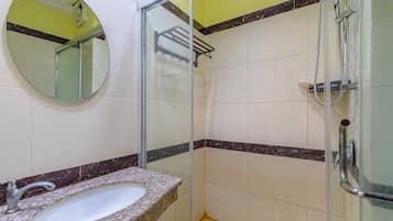 Un baño con lavamanos de encimera de granito, cabina de ducha de vidrio y un espejo en la pared.