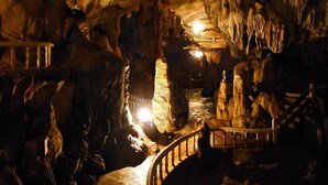 Una cova amb estalactites i estalagmites, un camí de fusta i una petita bassa.